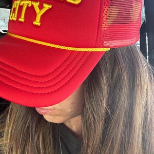 May include: Red and yellow trucker hat with the text "Kansas City" embroidered on the front.