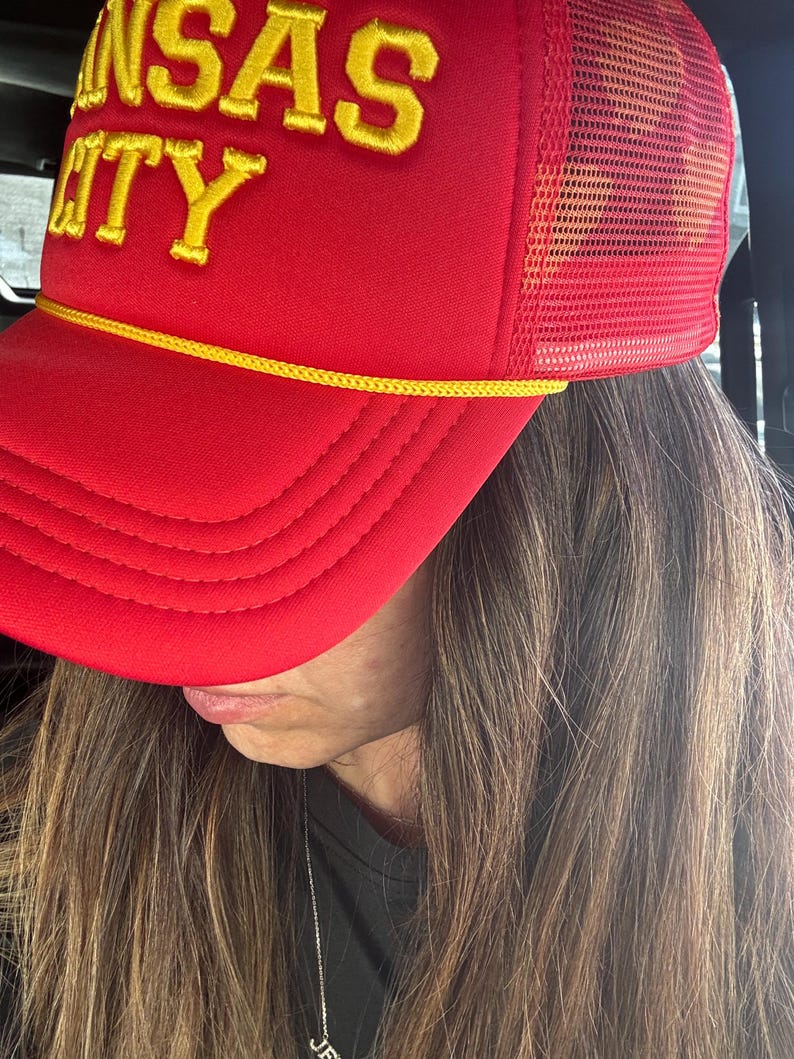 May include: Red and yellow trucker hat with the text "Kansas City" embroidered on the front.