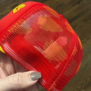 May include: Red mesh trucker hat with a yellow logo. The mesh is orange and red.