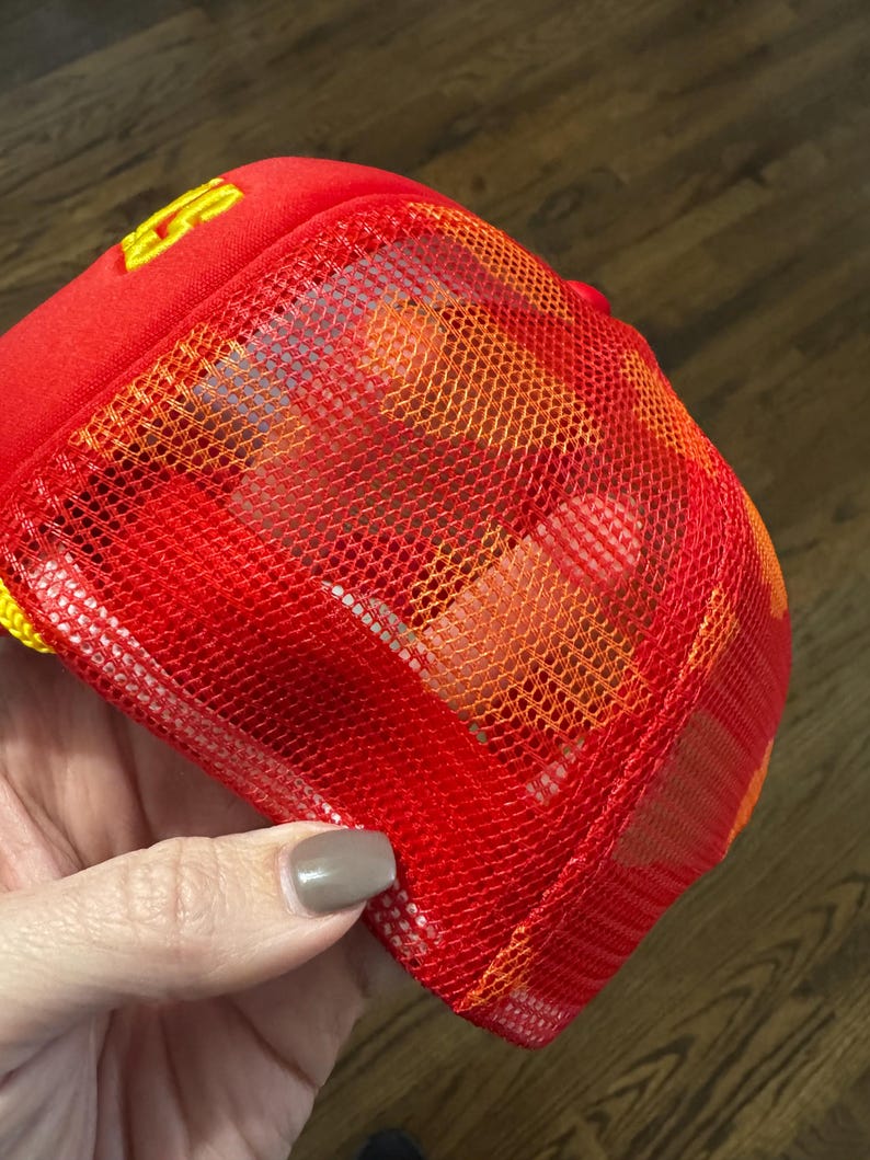 May include: Red mesh trucker hat with a yellow logo. The mesh is orange and red.