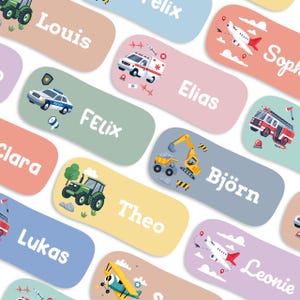 May include: A collection of colorful name tags with various illustrations. Each tag features a different name in white text and a cartoon image of a vehicle, such as a police car, ambulance, or airplane. The tags are in pastel colors.