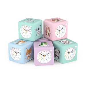May include: A collection of cube-shaped children's clocks in various pastel colors. Each clock face displays the time, and the sides feature illustrations of a fox, panda, unicorn, astronaut, and dinosaur. The clocks are designed for kids.
