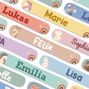 Può includere: Etichette colorate con nomi e illustrazioni di animali, arcobaleni e stelle. Ogni etichetta presenta un nome diverso, come "Lukas", "Marie" e "Felix". Le etichette sono in vari colori pastello, tra cui rosa, giallo e blu.