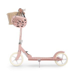 Può includere: Un monopattino rosa con ruote bianche e un casco abbinato. Un cestino in vimini è attaccato al manubrio. Lo scooter ha il marchio "Barenwerke" stampato sul telaio. Anche il casco è rosa.