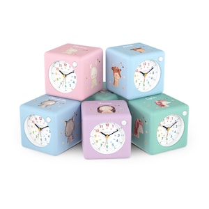 Könnte beinhalten: Eine Sammlung farbenfroher, würfelförmiger Wecker. Jede Uhr hat ein weißes Zifferblatt mit schwarzen Zahlen und Zeigern. Die Uhren sind pastellrosa, blau, lila und grün, mit Tierillustrationen und Namen wie "Jonas" und "Lynn".