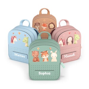 Könnte beinhalten: Fünf farbenfrohe Kinderrucksäcke. Jeder Rucksack zeigt eine andere Tierillustration und einen Namen: Matteo, Sophia und Hannah. Die Rucksäcke sind in Blau-, Rosa-, Grün- und Beigetönen gehalten.