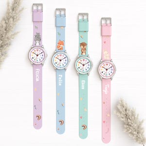 Pode incluir: Quatro relógios analógicos com pulseiras de silicone nas cores lavanda, azul claro, verde menta e rosa. Cada relógio possui um mostrador branco com números coloridos, caixa prateada e nomes personalizados: Felicia, Felix, Elias e Tanya.