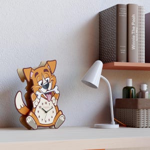 May include: A novelty dog-shaped clock, holding a bone. The clock face has black numerals and hands, with the brand name "Cander". The clock is brown, tan, and white, and sits on a desk next to a white lamp and books. The clock's dimensions are in centimeters.