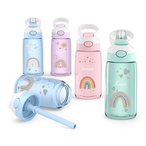 Peut inclure: Plusieurs gourdes colorées avec des motifs d'arc-en-ciel et de cœurs. Chaque gourde porte un nom différent : Moritz, Merle, Jonas et Lana. Les gourdes sont bleues, roses et vertes, avec des couvercles et des poignées blancs. Une gourde est ouverte, montrant la paille.