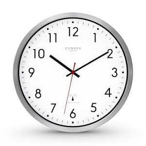 Könnte beinhalten: Eine weiße analoge Uhr mit schwarzen Zahlen und Zeigern. Die Uhr hat einen silbernen Metallrahmen und ist mit "CANDER BERLIN" beschriftet. Die Uhr ist Funksteuerbar und hat ein kleines Symbol einer Funkwelle.