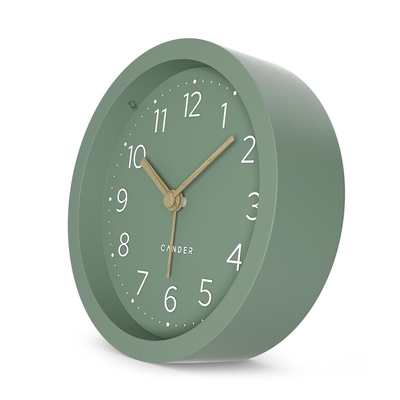 May include: A sage green analog clock with a round face. The clock has a white dial with black numerals and gold-colored hands. The word "CANDER" is printed in the center of the clock face.