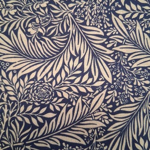 May include: Close-up of a fabric with a repeating floral pattern. The design features cream-coloured leaves, flowers, and vines against a dark navy blue background. The pattern is detailed and intricate, creating a classic, elegant look.