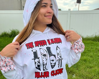 Könnte beinhalten: Weißer Kapuzenpullover mit roten Spritzern. Die Vorderseite des Pullovers zeigt eine schwarz-weiße Grafik eines Messers, einer Hockeymaske und einer Schrei-Maske mit dem Text "The Speed Walking Killer Cliche".