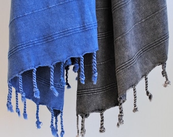 Könnte beinhalten: Zwei türkische Handtücher, eines blau und eines grau, mit Fransen an den Rändern. Die Handtücher hängen an einem Haken.