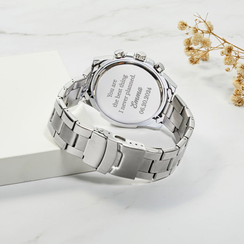 Puede incluir: Reloj plateado con una correa de acero inoxidable. La parte posterior del reloj tiene un mensaje grabado que dice: "You are the best thing I never planned. Emma 06.20.2024"