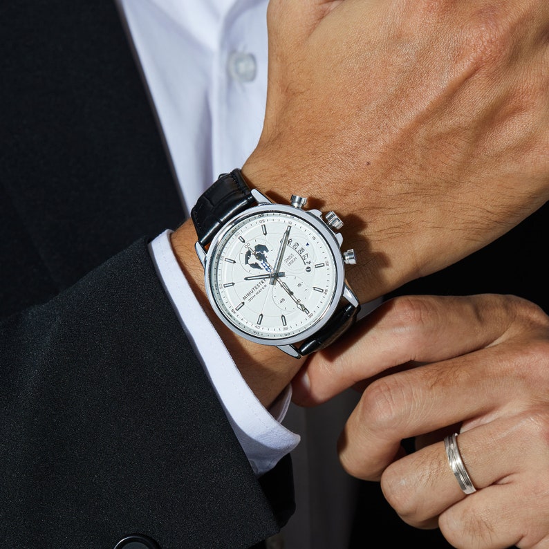 May include: A silver wristwatch with a white face and black leather band. The watch features a chronograph, date display, and a globe design on the face. The text "MONOCHROME" is printed on the face.