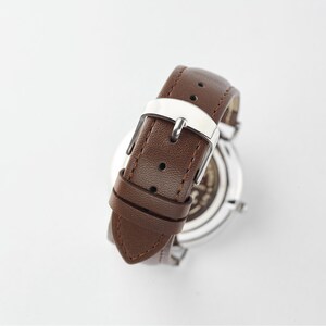 Close-up of a brown leather watch strap showing the silver buckle and stitching detail on the strap
