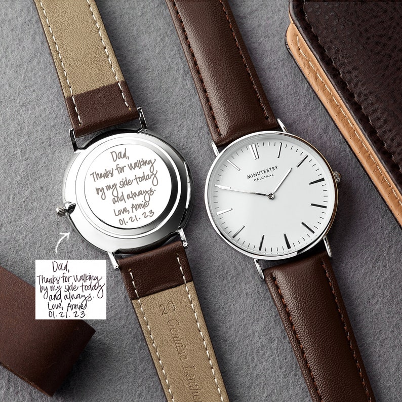 Wristwatch with a brown leather strap, alongside a personalized engraving on the back. The engraving is custom handwritten and reads: Dad, Thanks for walking by my side today and always. Love, Annie 01.21.23