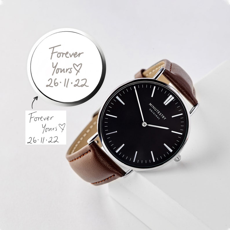 Brown leather wristwatch with a black minimalist face, showing an engraved message on the back reading Forever Yours, 26-11-22 with a heart symbol, featuring handwritten customization