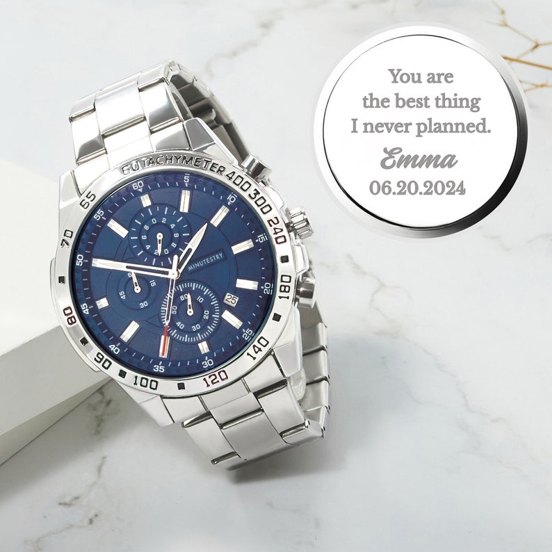 Puede incluir: Un reloj cron&oacute;grafo plateado con una esfera azul y una correa plateada. El reloj tiene una escala de taqu&iacute;metro alrededor del borde exterior de la esfera. El reloj est&aacute; sobre una superficie blanca. Un disco plateado con el texto "You are the best thing I never planned. Emma 06.20.2024" est&aacute; en el fondo.