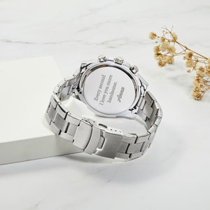May include: Silver watch with a stainless steel band. The back of the watch has an engraved message that reads "Every second I love you more handsome. Anna."