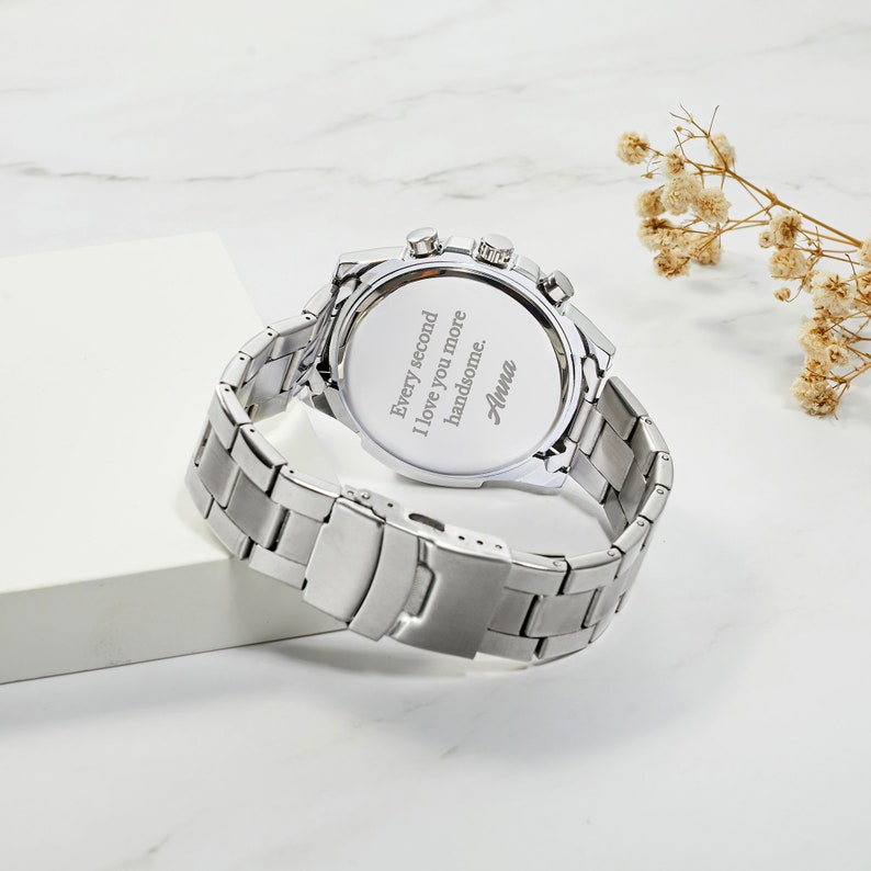 May include: Silver watch with a stainless steel band. The back of the watch has an engraved message that reads "Every second I love you more handsome. Anna."