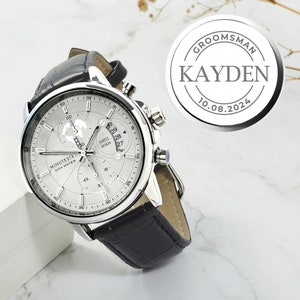 May include: A silver watch with a black leather band. The watch face has a white background with black markings and a small world map design. The watch has a date window and a chronograph function. The watch is labeled "MINUTESTR 30M WATER".