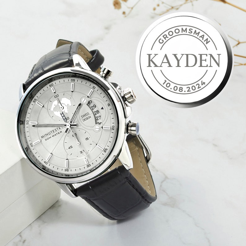 May include: A silver watch with a black leather band. The watch face has a white background with black markings and a small world map design. The watch has a date window and a chronograph function. The watch is labeled "MINUTESTR 30M WATER".