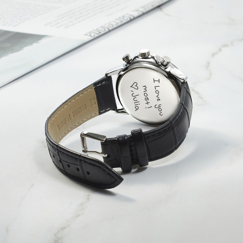 May include: Black leather wristwatch with a silver face and a personalized message on the back that reads "I love you most! &hearts; Julia".