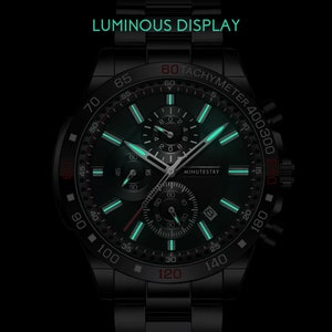 Puede incluir: Un reloj de pulsera cron&oacute;grafo negro con una esfera verde luminosa y detalles rojos. El reloj tiene una escala de taqu&iacute;metro alrededor del borde exterior y las palabras "MINUTESTRY" impresas en la esfera.