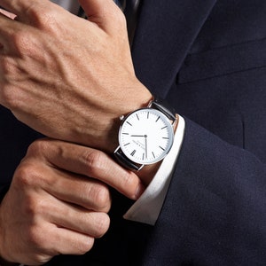 Man adjusting his classic watch with black leather strap and minimalist design.