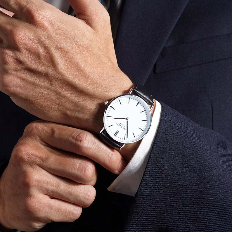 Man adjusting his classic watch with black leather strap and minimalist design.