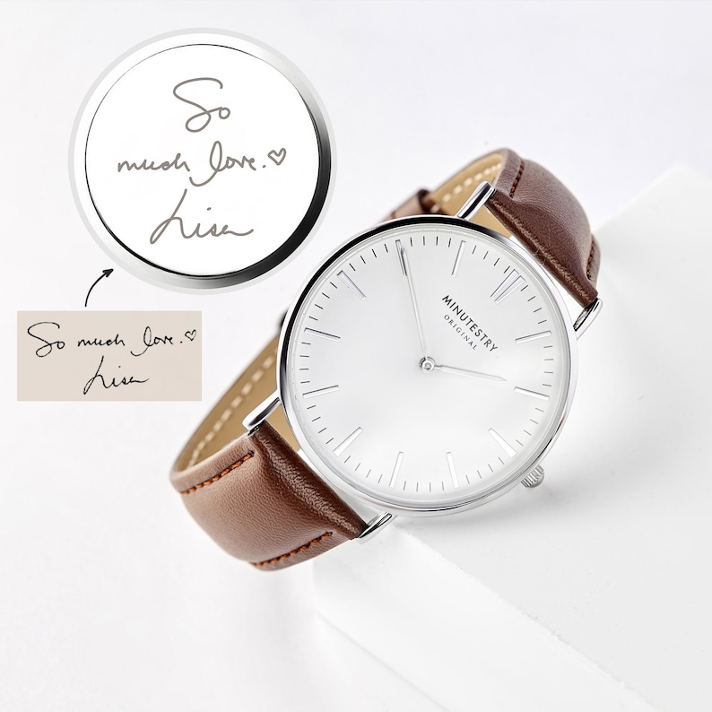A minimalist watch with a brown leather strap and a white dial, featuring a custom handwritten message on the back saying So much love, Lisa engraved in a script font