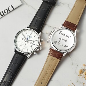 May include: Two wristwatches with black and brown leather bands. The watch on the left has a white face with a world map design and the words "MINUTEST". The watch on the right has a silver face with the words "forever yours 9.14.24" written on it.