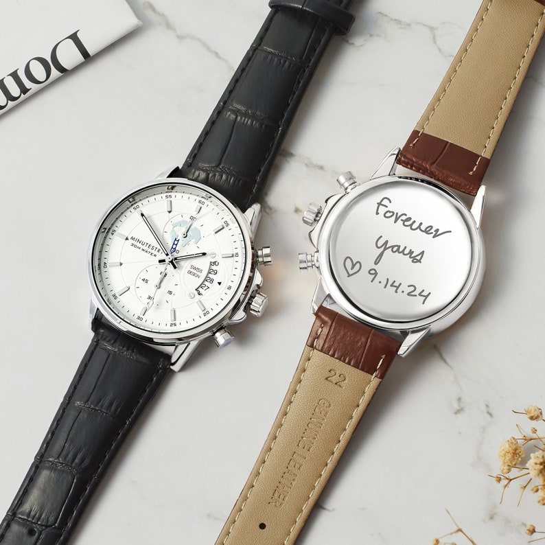 May include: Two wristwatches with black and brown leather bands. The watch on the left has a white face with a world map design and the words "MINUTEST". The watch on the right has a silver face with the words "forever yours 9.14.24" written on it.