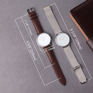 May include: Two wristwatches with white faces and silver hands. The watch on the left has a brown leather band, and the watch on the right has a silver mesh band. Both watches are 1 1/2 inches in diameter.