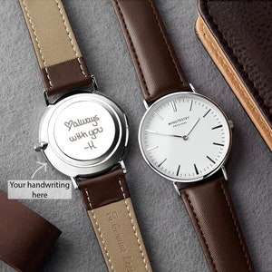 A minimalist watch with a brown leather strap, featuring a custom handwritten message on the back reading Always with you - H engraved in script