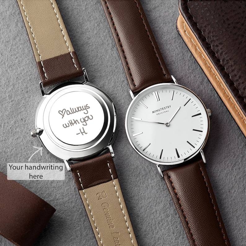 A minimalist watch with a brown leather strap, featuring a custom handwritten message on the back reading Always with you - H engraved in script