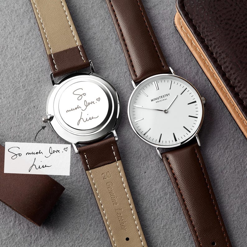 Two wristwatches with brown leather straps displayed side by side, one showing the engraved message So much love. Lisa on the back, featuring handwritten customization