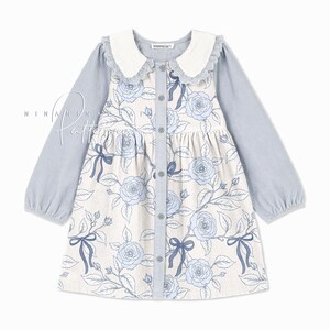 May include: A light blue corduroy dress with a white collar and long sleeves. The dress has a floral print with blue roses and bows. The dress has a button-up front.
