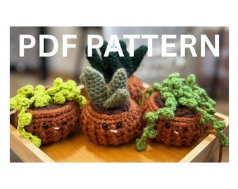 May include: Three crocheted plant pots with smiling faces and green plant details. The pots are brown with green and brown plant details. The text "PDF PATTERN" is in white letters at the top of the image.