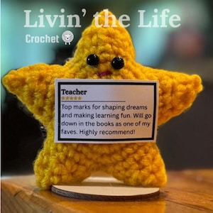 May include: A yellow crocheted star with black button eyes and a small pink mouth. It holds a white card with the word "Teacher" and a positive review. The text "Livin' the Life Crochet" is at the top. The star is handmade.