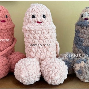 May include: Three crocheted plush toys in the shape of a person. The toys are in the colors terra cotta, cameo rose, and toasted birch. Each toy has a face with black eyes and a red mouth.