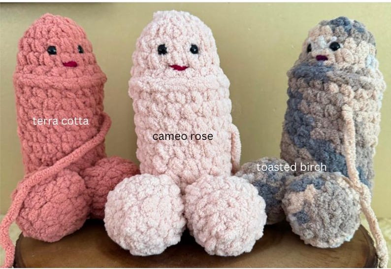 May include: Three crocheted plush toys in the shape of a person. The toys are in the colors terra cotta, cameo rose, and toasted birch. Each toy has a face with black eyes and a red mouth.