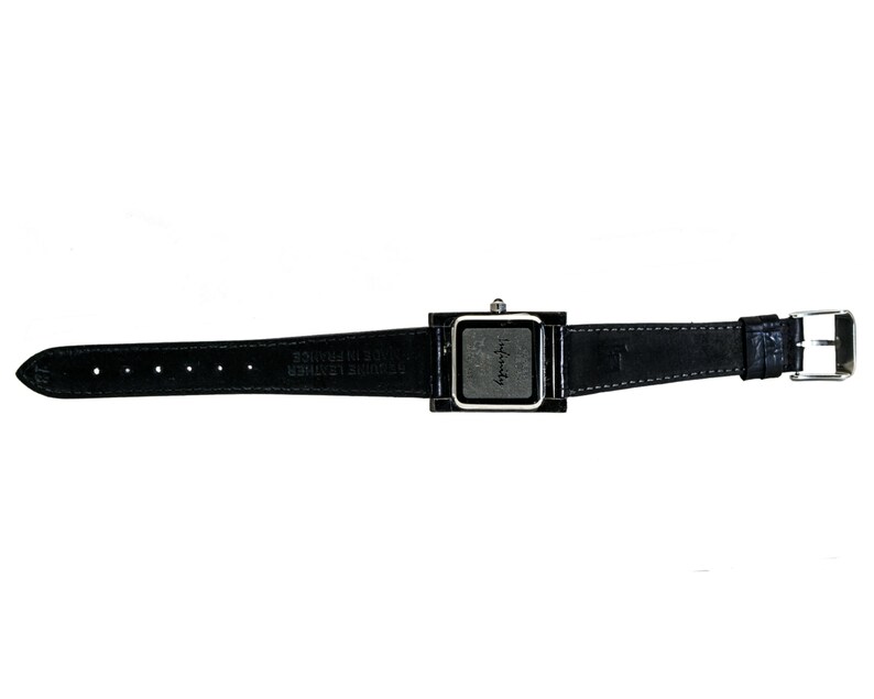 Peut inclure: Une montre-bracelet noire avec un cadran carr&eacute; et un bracelet en cuir noir. Le cadran de la montre est argent&eacute; avec un centre gris fonc&eacute;. Le bracelet a une boucle argent&eacute;e et est fix&eacute; au cadran par un cadre noir.