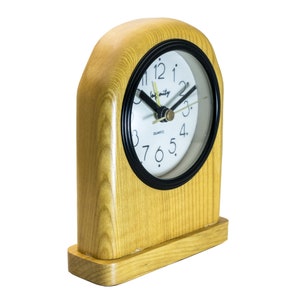 Pode incluir: Um despertador de madeira com um mostrador branco e ponteiros pretos. O relógio tem uma moldura preta e as palavras "for unity" são impressas no mostrador. O relógio está em uma base de madeira.