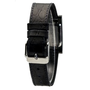 Peut inclure: Une montre-bracelet noire avec un cadran rectangulaire et un bracelet en cuir noir. Le bracelet pr&eacute;sente un motif textur&eacute; et une boucle argent&eacute;e. La montre est pr&eacute;sent&eacute;e sur fond blanc.