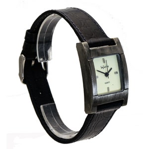 Peut inclure: Une montre-bracelet rectangulaire avec un bracelet en cuir noir et une boucle argent&eacute;e. Le cadran de la montre est carr&eacute; avec un fond clair et des aiguilles noires. Le bo&icirc;tier de la montre est de couleur m&eacute;tallique fonc&eacute;e, et le mot "Infinity" est imprim&eacute; sur le cadran.