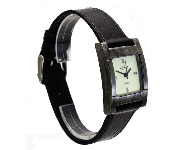 Peut inclure: Une montre-bracelet rectangulaire avec un bracelet en cuir noir et une boucle argent&eacute;e. Le cadran de la montre est carr&eacute; avec un fond clair et des aiguilles noires. Le bo&icirc;tier de la montre est de couleur m&eacute;tallique fonc&eacute;e, et le mot "Infinity" est imprim&eacute; sur le cadran.