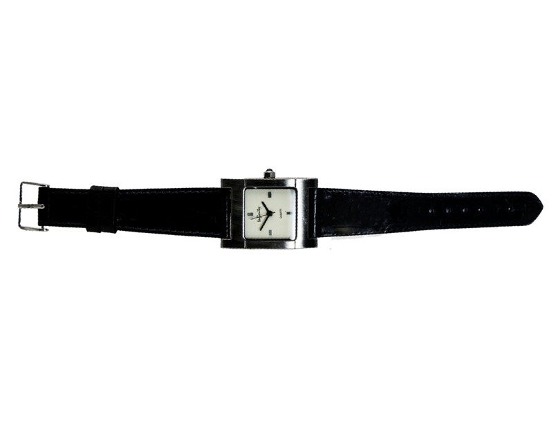 Peut inclure: Une montre-bracelet argent&eacute;e avec un cadran carr&eacute; et un bracelet en cuir noir. La montre a un cadran blanc avec des aiguilles et des marqueurs noirs. Le bracelet mesure environ 23 cm de long.